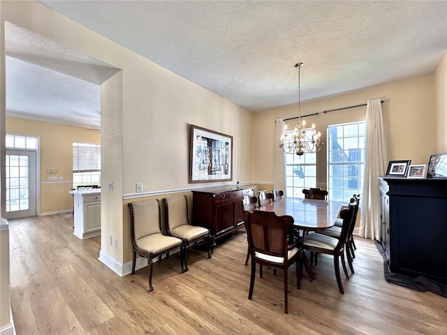dining space featuring a textured ceiling, a notable chandelier, light wood-style flooring, and baseboards