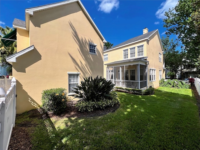 rear view of property featuring a sunroom, a lawn, stucco siding, and fence