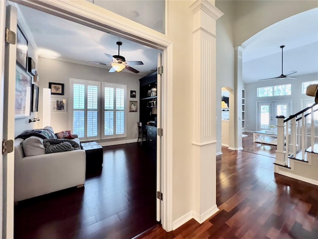 hall featuring baseboards, arched walkways, stairway, dark wood-style floors, and ornate columns