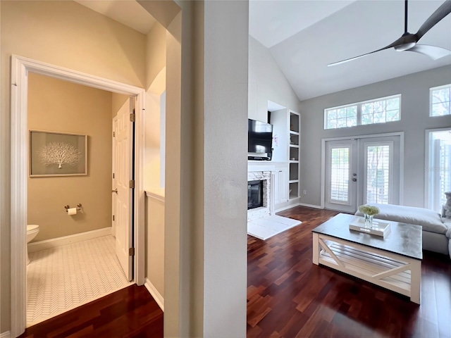 living area featuring baseboards, wood finished floors, ceiling fan, and a stone fireplace