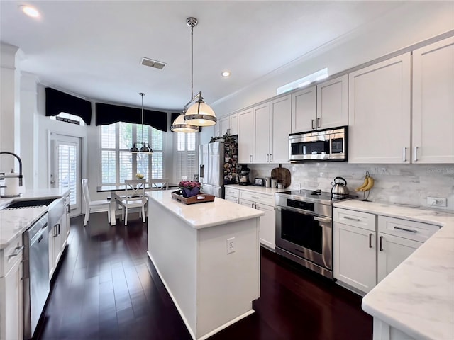 kitchen featuring dark wood-style floors, a sink, stainless steel appliances, tasteful backsplash, and light stone counters