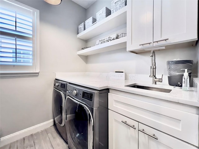 laundry room with independent washer and dryer, cabinet space, light wood finished floors, a sink, and baseboards