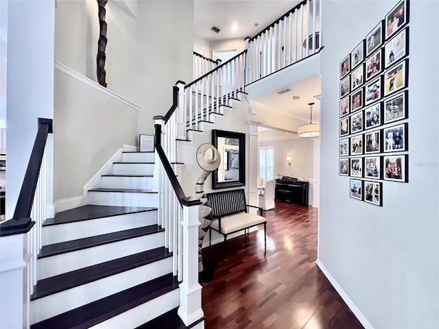 staircase with a towering ceiling, wood finished floors, visible vents, and baseboards
