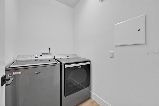 washroom featuring washing machine and clothes dryer, light wood-style flooring, laundry area, and baseboards