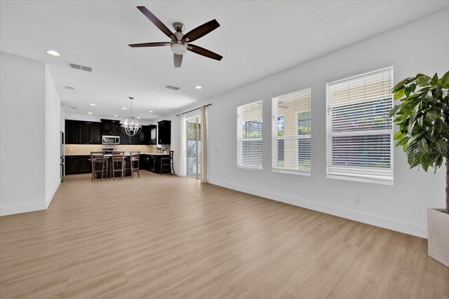 living area with visible vents, light wood-type flooring, baseboards, and ceiling fan with notable chandelier