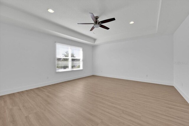 unfurnished room featuring recessed lighting, a raised ceiling, a ceiling fan, light wood-style flooring, and baseboards