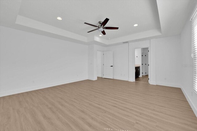 unfurnished bedroom with baseboards, recessed lighting, light wood finished floors, and a tray ceiling