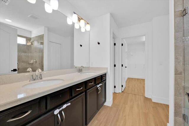 full bathroom with double vanity, wood finished floors, a shower stall, and a sink