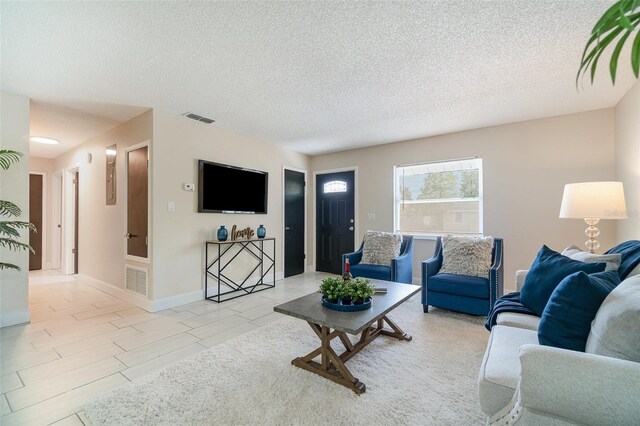living area featuring baseboards, visible vents, and a textured ceiling