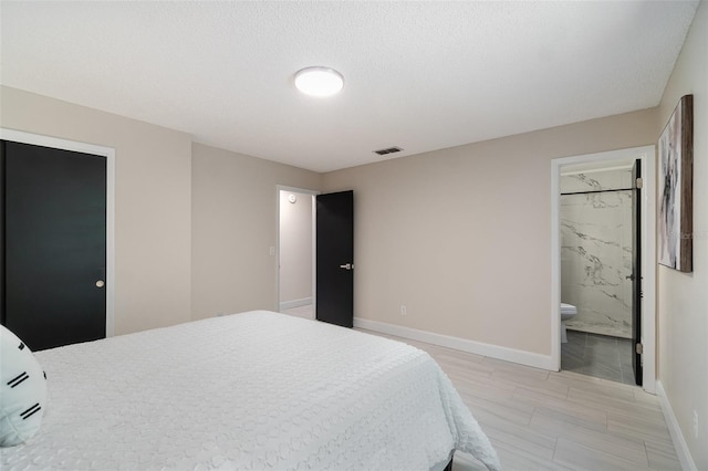 bedroom with wood finish floors, visible vents, ensuite bath, and baseboards
