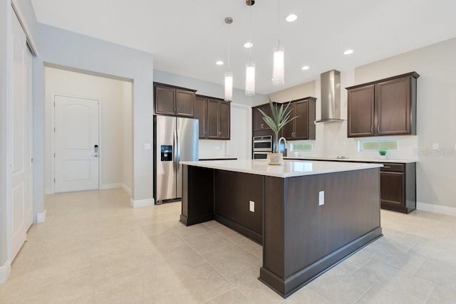 kitchen with a large island, dark brown cabinets, light countertops, stainless steel fridge, and wall chimney exhaust hood