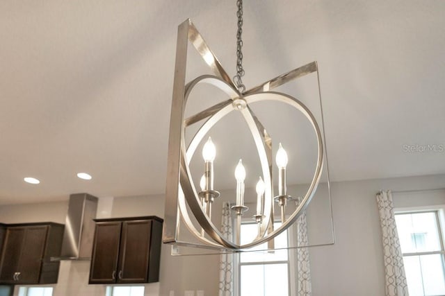 room details with dark brown cabinets, an inviting chandelier, recessed lighting, and wall chimney exhaust hood