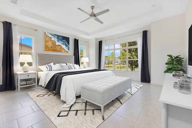 bedroom with light tile patterned flooring, a tray ceiling, and multiple windows