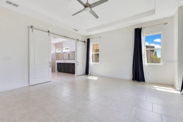 unfurnished room featuring ceiling fan, visible vents, a barn door, and plenty of natural light