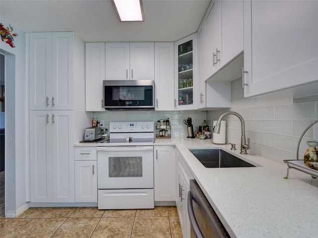 kitchen featuring white cabinetry, stainless steel appliances, glass insert cabinets, and a sink