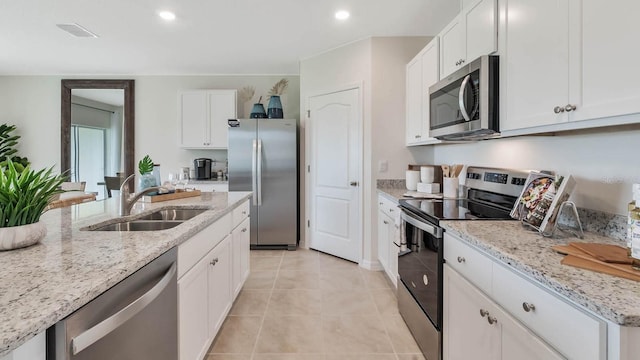 kitchen with light stone countertops, a sink, stainless steel appliances, visible vents, and white cabinets