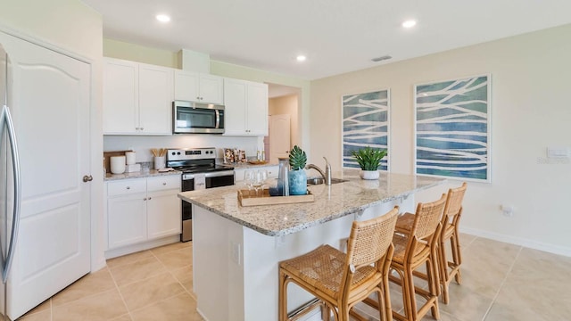 kitchen with light stone counters, a kitchen breakfast bar, white cabinets, and appliances with stainless steel finishes