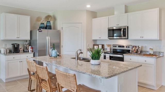 kitchen with light stone counters, light tile patterned floors, white cabinetry, a sink, and appliances with stainless steel finishes