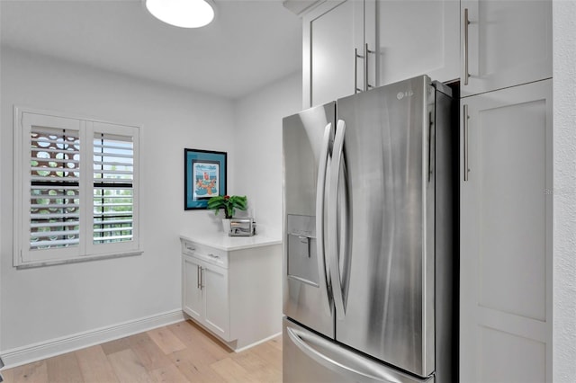 kitchen featuring white cabinets, light wood finished floors, stainless steel fridge with ice dispenser, light countertops, and baseboards