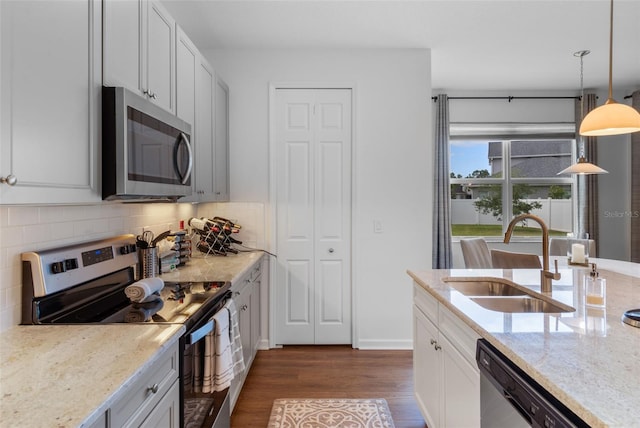 kitchen featuring light stone counters, a sink, stainless steel appliances, tasteful backsplash, and dark wood-style floors