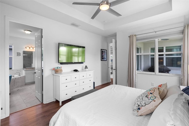 bedroom with ceiling fan, visible vents, a raised ceiling, dark wood-style floors, and connected bathroom