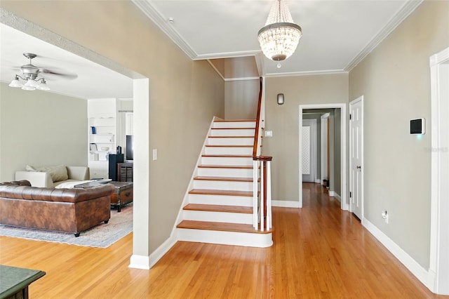 stairs with crown molding, baseboards, wood finished floors, and ceiling fan with notable chandelier