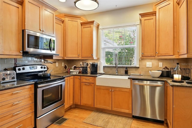 kitchen with appliances with stainless steel finishes, tasteful backsplash, light wood-style flooring, and a sink