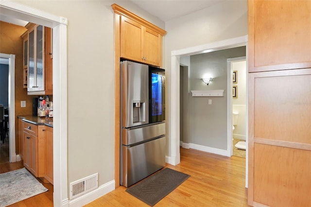 kitchen with visible vents, stainless steel fridge, glass insert cabinets, and light wood finished floors