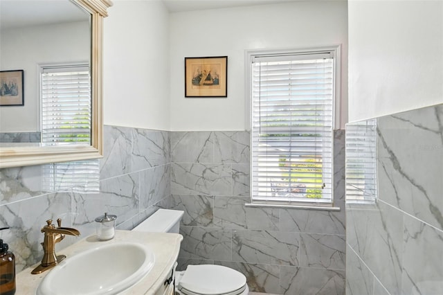 bathroom with tile walls, toilet, vanity, and plenty of natural light