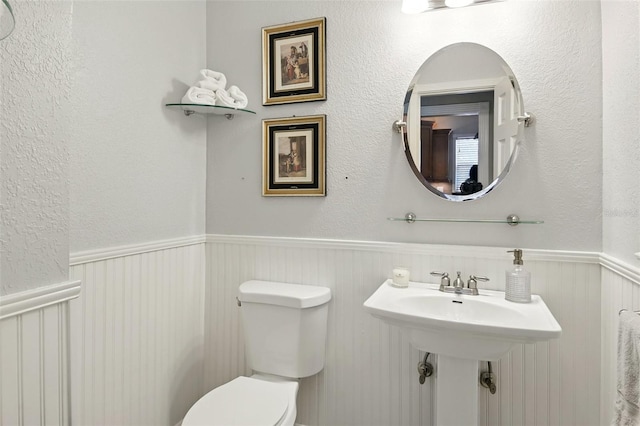 half bath with toilet and a wainscoted wall