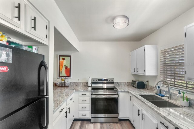 kitchen featuring stainless steel electric range, wood finished floors, a sink, freestanding refrigerator, and white cabinetry