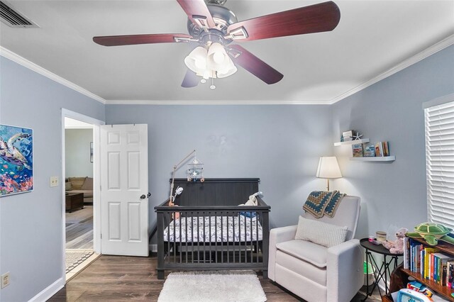 bedroom with ceiling fan, visible vents, a nursery area, wood finished floors, and ornamental molding