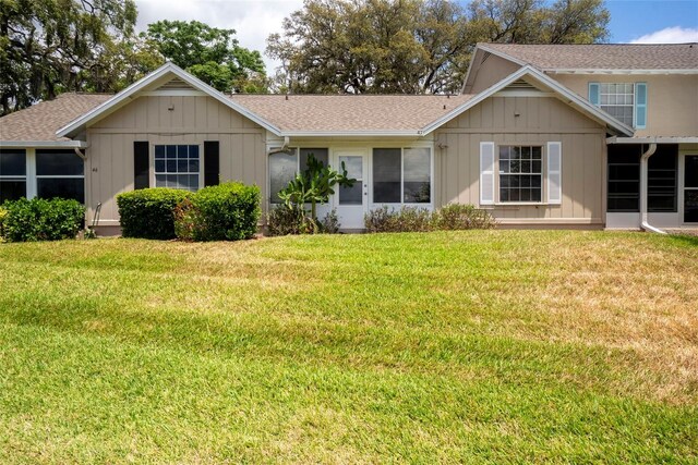 view of front of house with board and batten siding, a shingled roof, and a front lawn