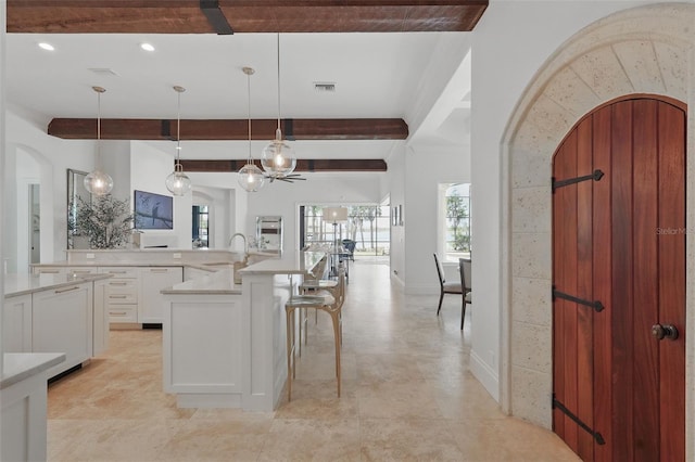 5550 Osprey Isle Ln, Orlando, FL 32819 - kitchen with visible vents, arched walkways, beam ceiling, a sink, and white cabinets