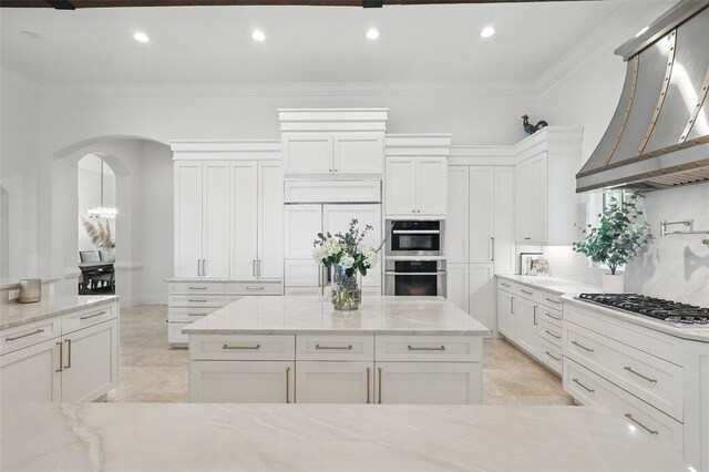 5550 Osprey Isle Ln, Orlando, FL 32819 - kitchen with gas cooktop, crown molding, arched walkways, white cabinetry, and wall chimney exhaust hood