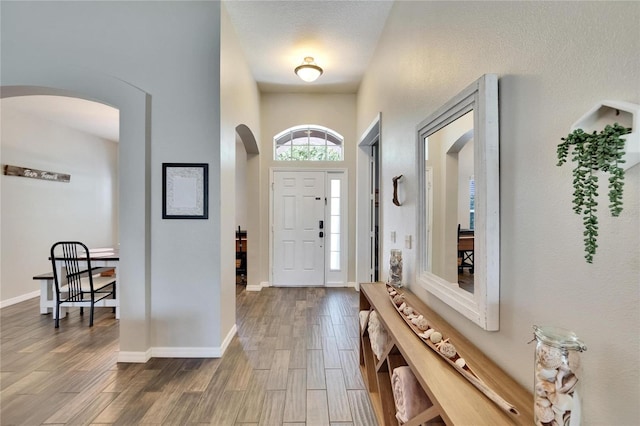 entrance foyer with arched walkways, baseboards, and wood finished floors