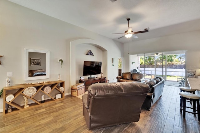 living room featuring wood finished floors, visible vents, baseboards, ceiling fan, and arched walkways