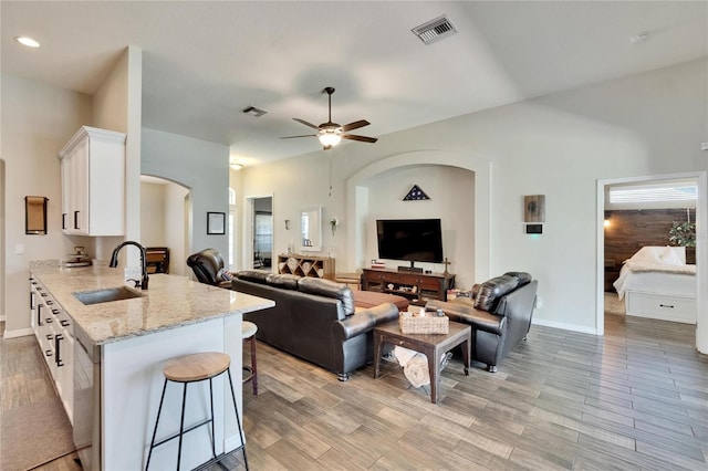 living room with light wood-style flooring, arched walkways, a ceiling fan, and visible vents