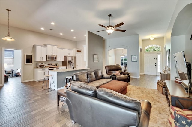 living room featuring light wood-style flooring, baseboards, ceiling fan, arched walkways, and recessed lighting