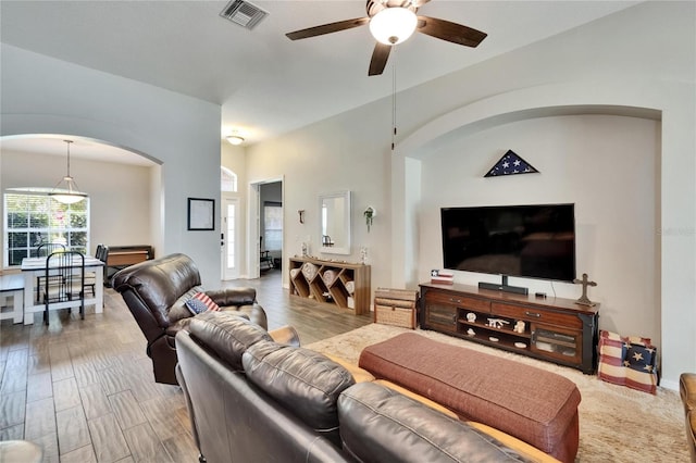 living room featuring ceiling fan, visible vents, wood finished floors, and arched walkways