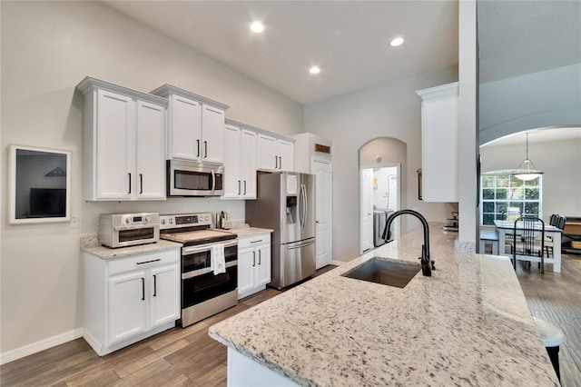 kitchen featuring wood finished floors, a sink, white cabinetry, arched walkways, and appliances with stainless steel finishes