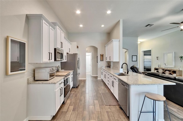 kitchen with a sink, stainless steel appliances, open floor plan, ceiling fan, and arched walkways