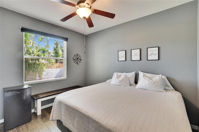 bedroom with light wood-type flooring, baseboards, a ceiling fan, and refrigerator