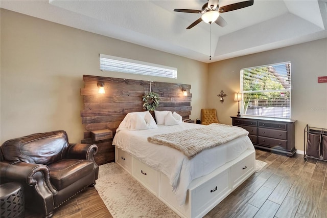 bedroom with a tray ceiling, ceiling fan, wood finished floors, and multiple windows