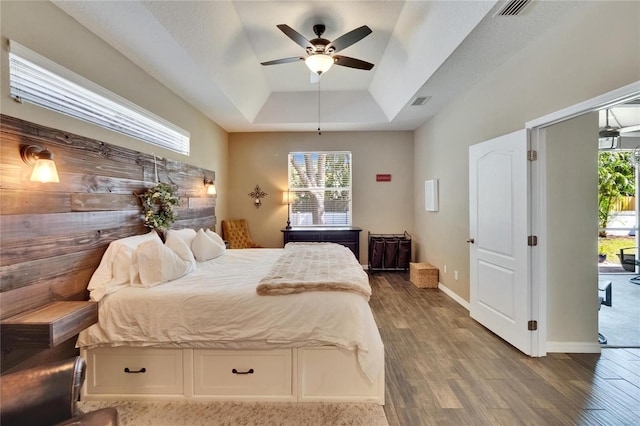 bedroom with a ceiling fan, a tray ceiling, visible vents, and wood finished floors