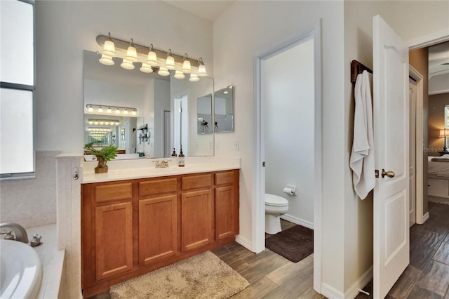 bathroom with toilet, wood finished floors, vanity, and tiled bath