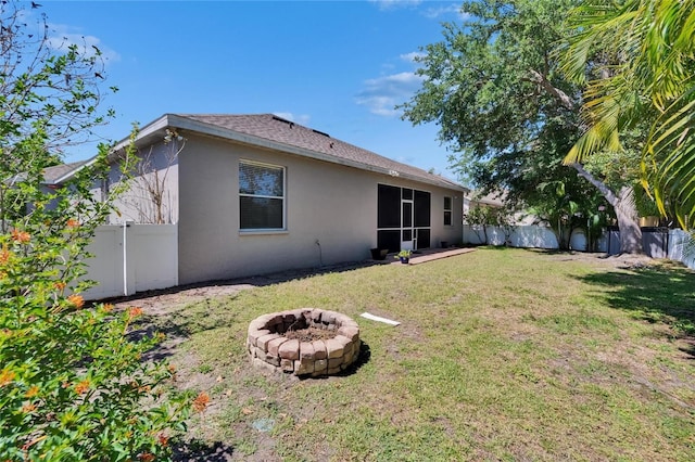 back of house with an outdoor fire pit, stucco siding, a fenced backyard, a yard, and roof with shingles