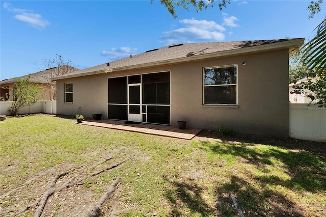 rear view of house featuring a yard, fence, a shingled roof, and stucco siding