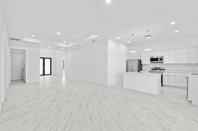 interior space with a kitchen island, open floor plan, a raised ceiling, white cabinets, and appliances with stainless steel finishes