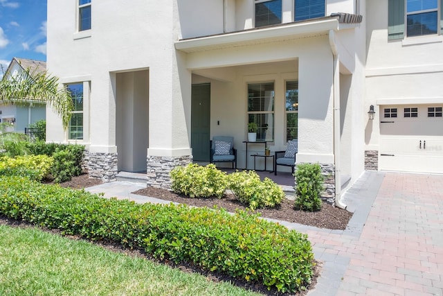 entrance to property with stucco siding, covered porch, stone siding, and a garage